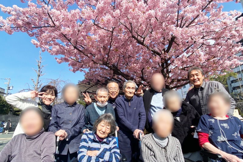 桜の前で集合写真に写る利用者さま