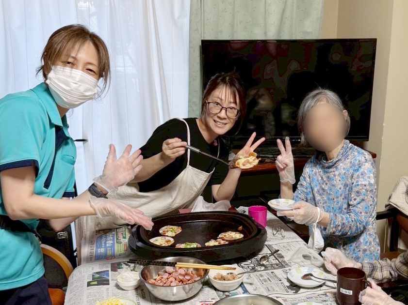 ホットプレートを囲んで笑顔のスタッフたちと利用者さま