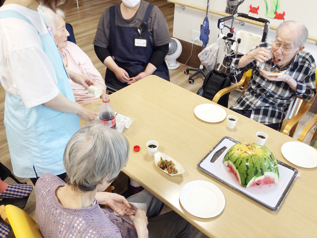 食卓を囲ってたこ焼きとスイカを食べる利用者さま