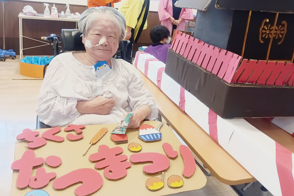 お神輿の横で「ちくさ なつまつり」の看板を持って記念撮影された利用者さま