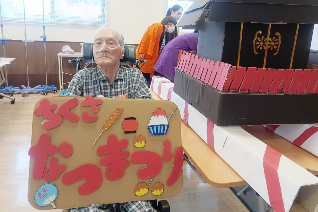 お神輿の横で「ちくさ なつまつり」の看板を持って記念撮影された利用者さま