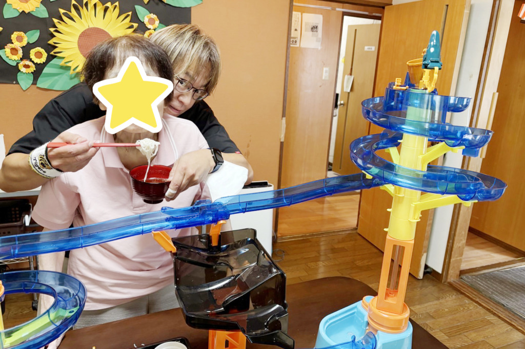 スタッフの補助を受けて流しそうめん器からそうめんを食べる利用者さま