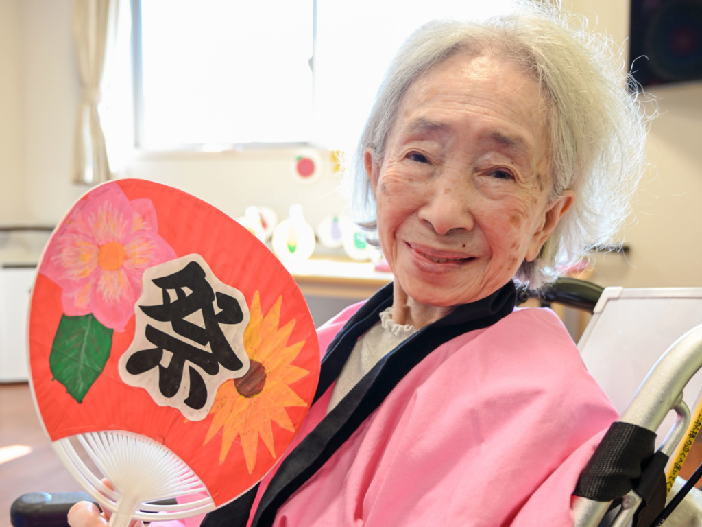「祭」のうちわを持って笑顔の、法被を着た利用者さま
