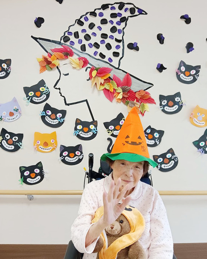 ハロウィンの壁飾りの前で写真に写った入居者さま