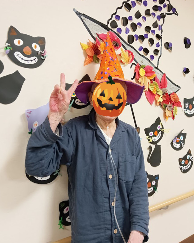 ハロウィンの壁飾りの前でピースする入居者さま