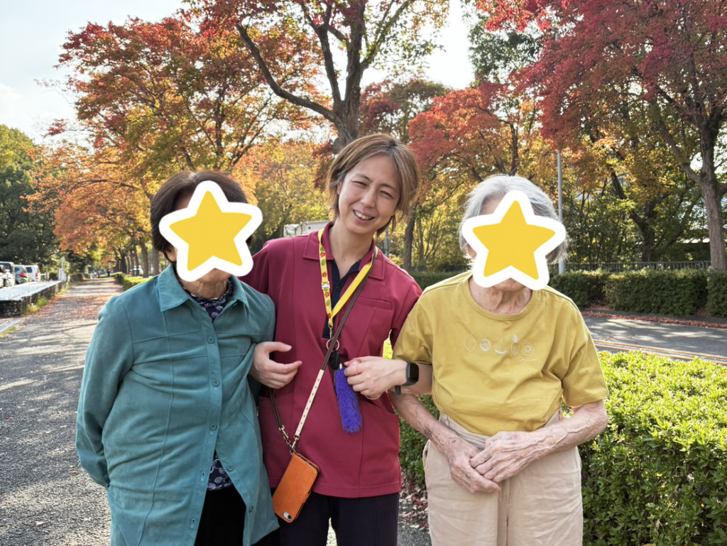 紅葉の下でスタッフを挟んで腕を組む利用者さまたち