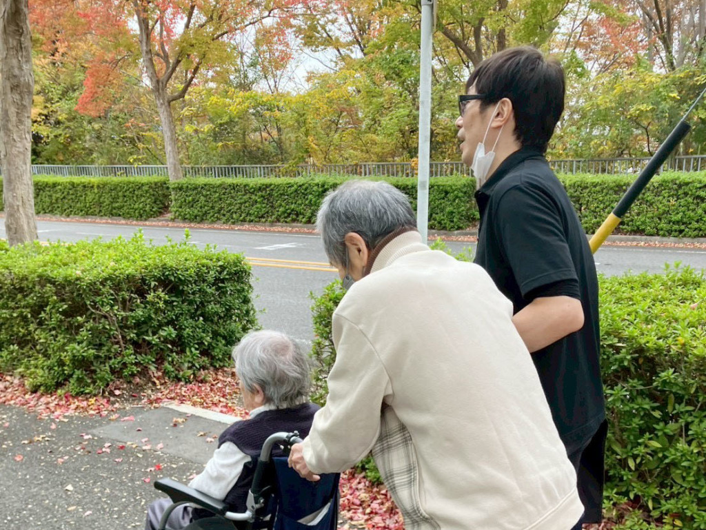 紅葉で色づいた道を歩く利用者さまたちとスタッフ