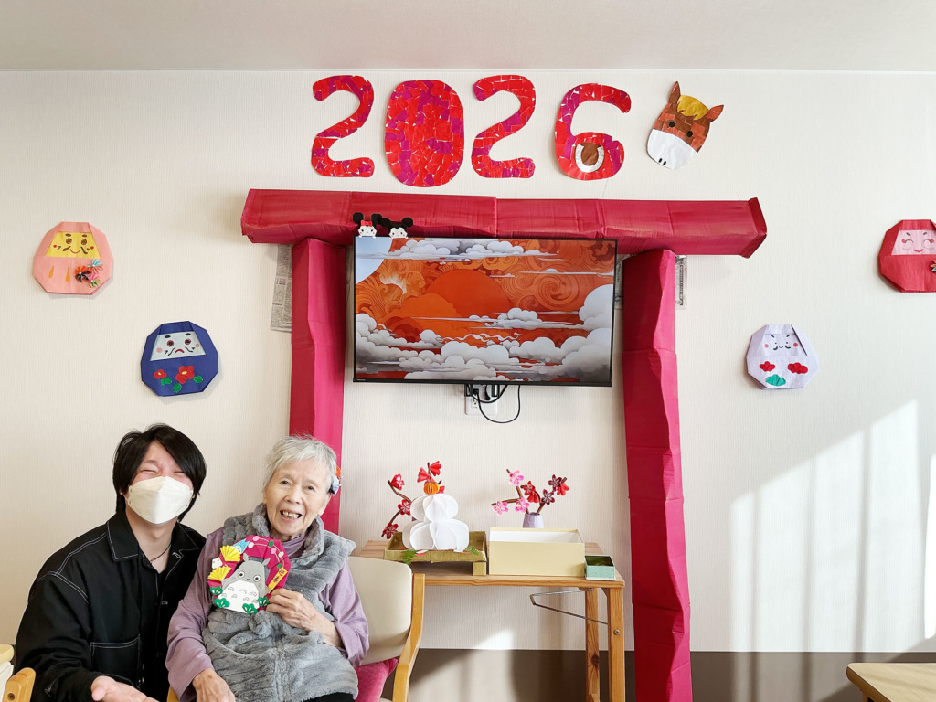 トトロの正月飾りを持ってスタッフと一緒に写真に写る入居者さま