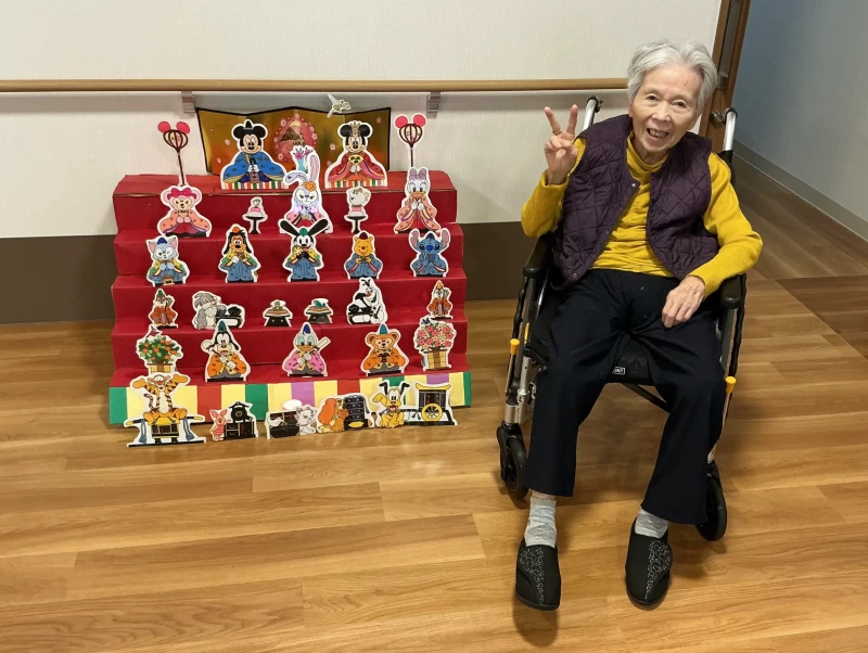 キャラクター物のひな壇の隣でピースをする入居者さま